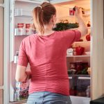 A woman opens the fridge to retrieve food items in a cozy kitchen setting.